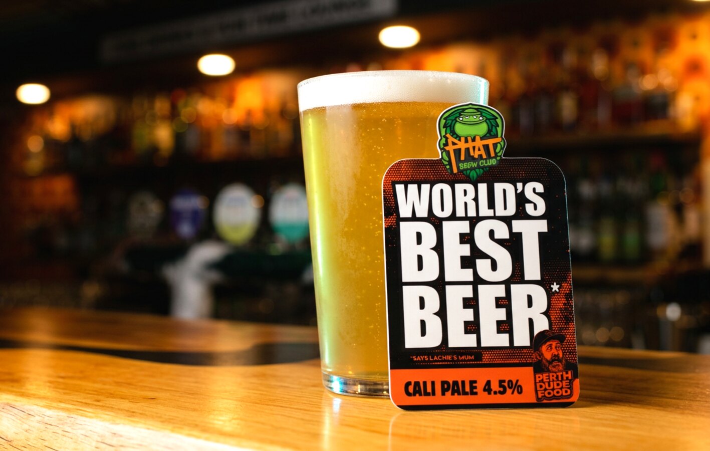 A pint of World's Best Beer on the timber bar at Planet Royale with the Phat Brew Club decal leaning against the glass.