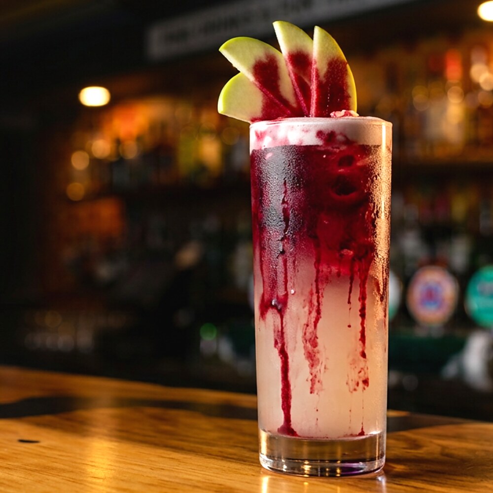 A Bloody Good Time cocktail in a tall glass, pale at the base with deep beetroot bleeding down through it and an apple fan garnish.