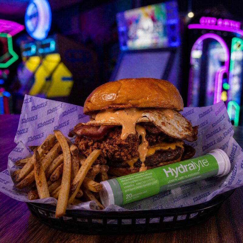 The Hangover Burger - fried chicken, beef patty, bacon, fried egg and oozing burger sauce stacked on a brioche bun, served with chips and a Hydralyte tablet.